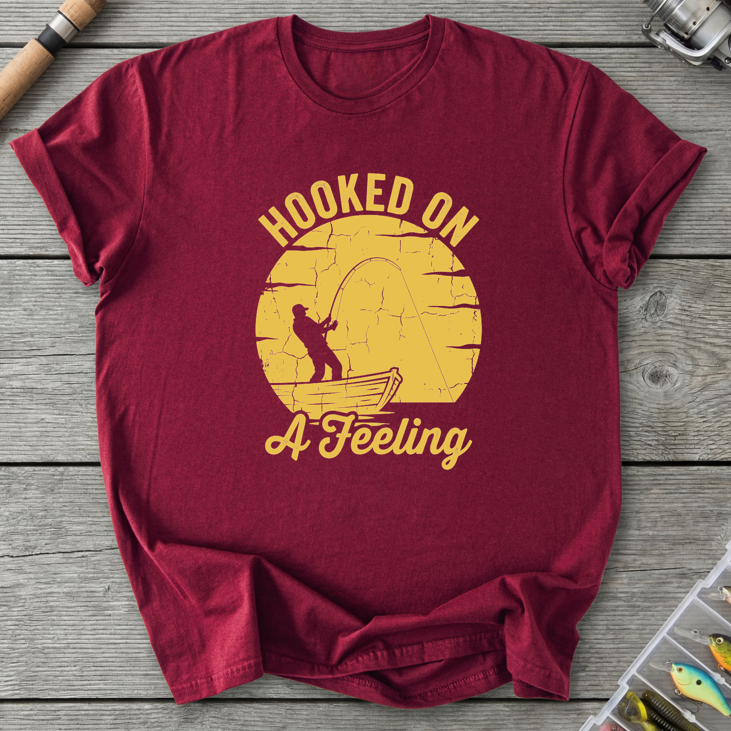 Maroon t-shirt with yellow graphic and text 'Hooked on a Feeling' on a wooden surface.
