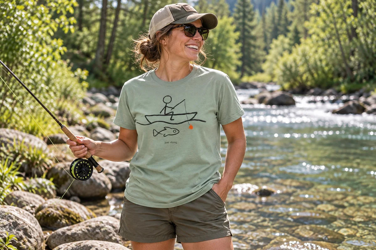 An angler wearing the Just Vibing fishing tee beside a forest stream.